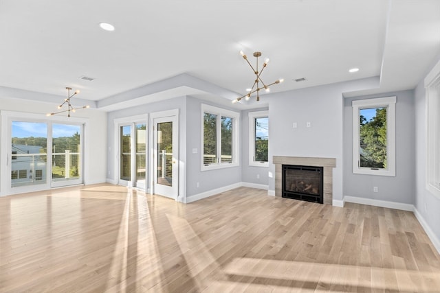 unfurnished living room featuring light hardwood / wood-style flooring, a tiled fireplace, and a notable chandelier