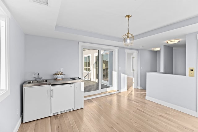 interior space featuring light wood-type flooring, sink, and a tray ceiling