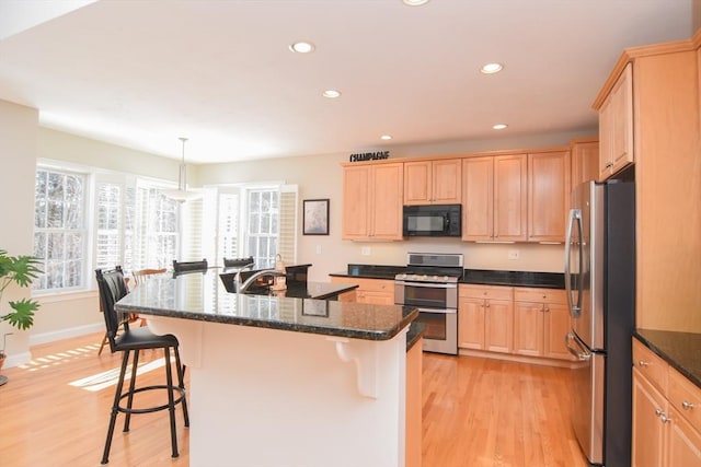 kitchen featuring stainless steel appliances, light brown cabinetry, a kitchen bar, and light wood-style flooring