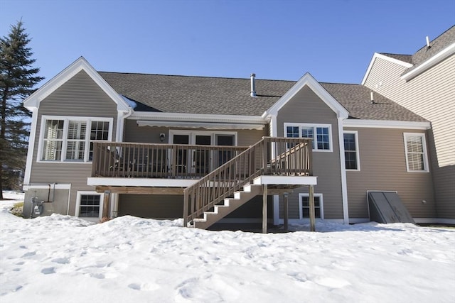 snow covered back of property with roof with shingles, a deck, and stairs