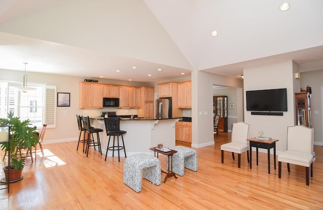 kitchen featuring a kitchen bar, light brown cabinets, black microwave, and freestanding refrigerator