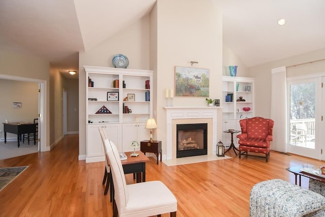 sitting room featuring high vaulted ceiling, a fireplace with flush hearth, light wood-style flooring, and baseboards