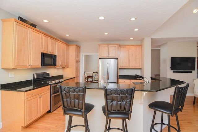 kitchen with light wood finished floors, recessed lighting, light brown cabinetry, appliances with stainless steel finishes, and a kitchen bar