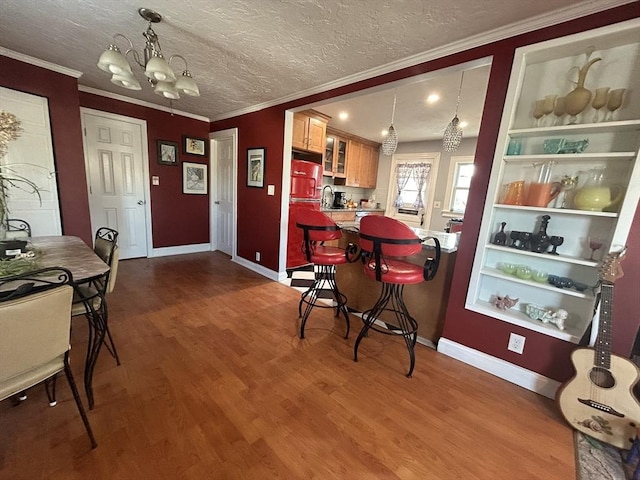 dining area with sink, crown molding, an inviting chandelier, a textured ceiling, and hardwood / wood-style floors