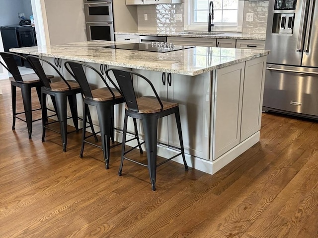 kitchen featuring appliances with stainless steel finishes, a kitchen breakfast bar, a center island, light stone countertops, and a sink