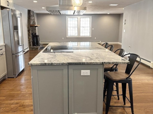 kitchen featuring island range hood, a kitchen island, a breakfast bar, black electric cooktop, and high end fridge