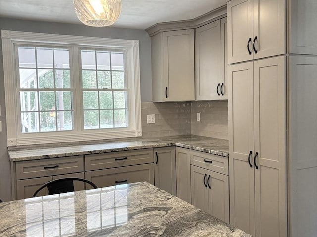 kitchen with tasteful backsplash, light stone counters, and gray cabinetry