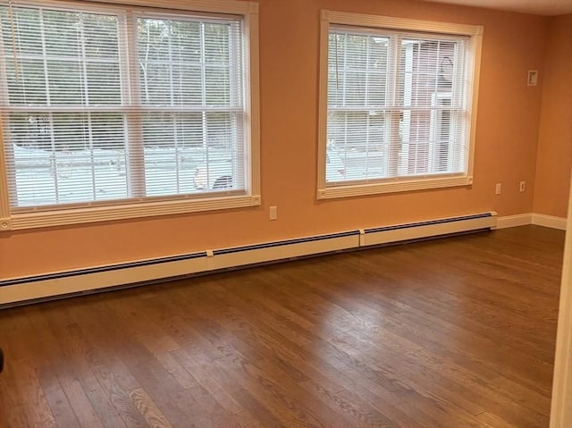 empty room featuring a baseboard heating unit, plenty of natural light, baseboards, and wood finished floors