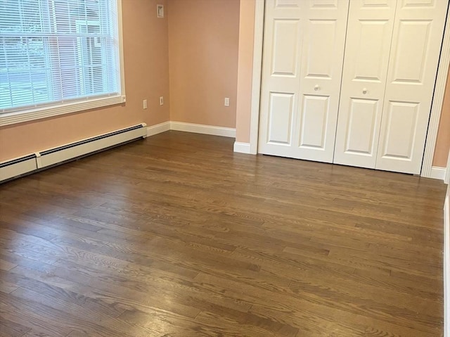 unfurnished bedroom featuring dark wood-type flooring, a closet, baseboards, and baseboard heating