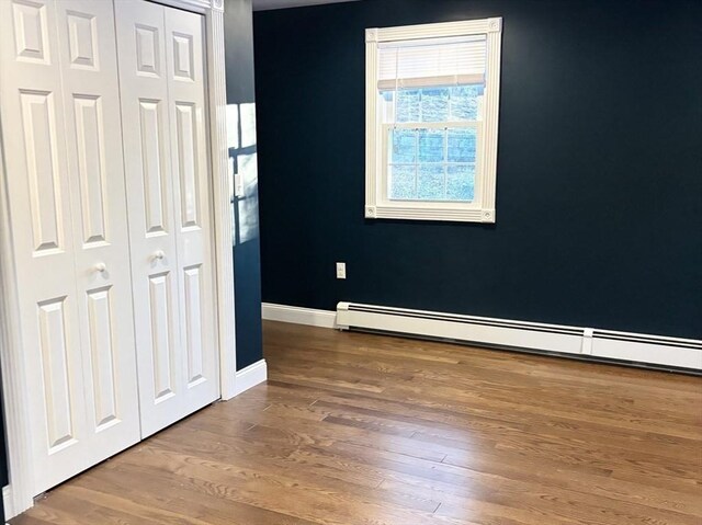 unfurnished bedroom featuring a baseboard radiator, a closet, baseboards, and wood finished floors