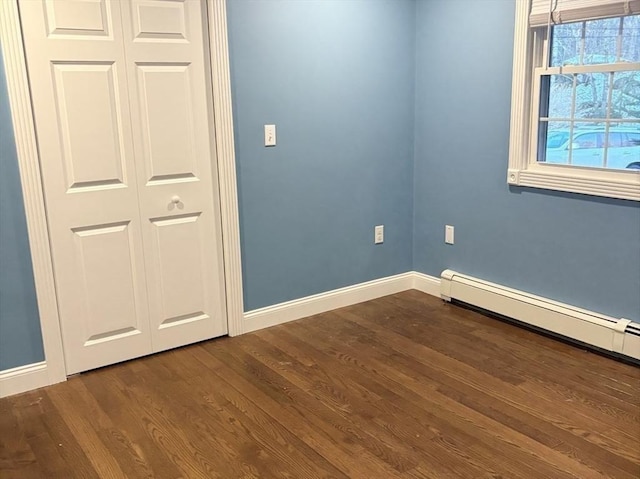 unfurnished room featuring baseboard heating, dark wood finished floors, and baseboards