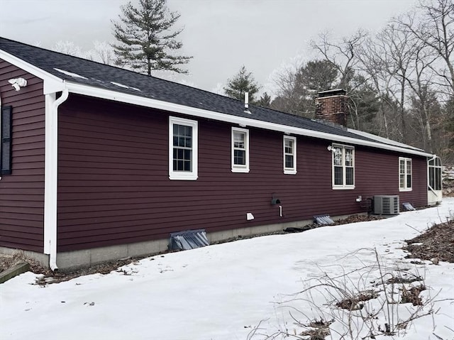 view of snowy exterior with a chimney and central air condition unit