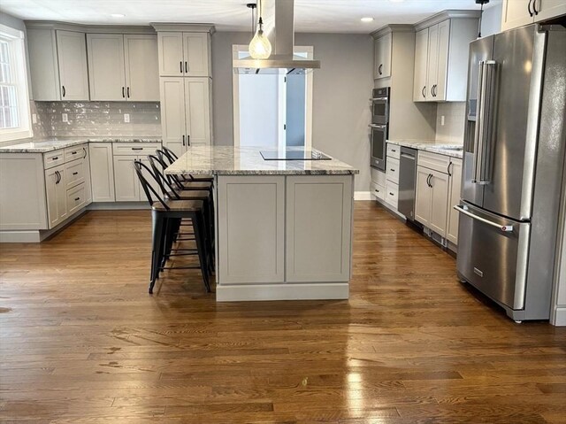 kitchen with light stone counters, island exhaust hood, hanging light fixtures, appliances with stainless steel finishes, and a kitchen island