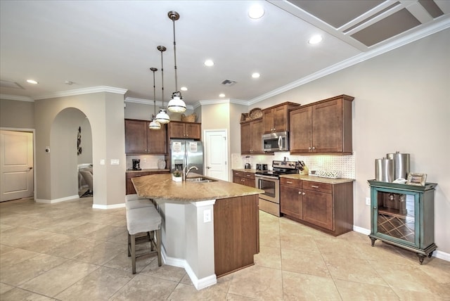 kitchen featuring a kitchen bar, stainless steel appliances, a center island with sink, tasteful backsplash, and ornamental molding