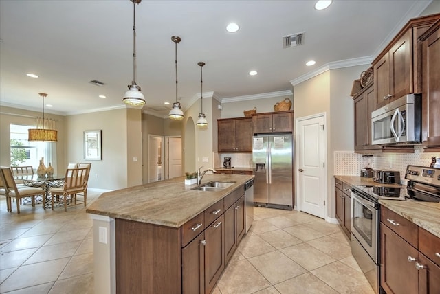 kitchen with ornamental molding, stainless steel appliances, hanging light fixtures, sink, and a kitchen island with sink