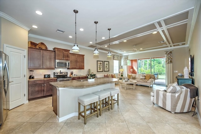 kitchen with a center island with sink, hanging light fixtures, tasteful backsplash, a breakfast bar, and appliances with stainless steel finishes