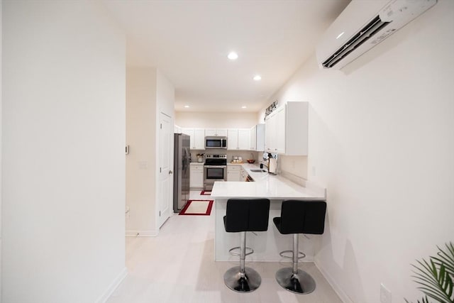 kitchen with white cabinets, appliances with stainless steel finishes, a kitchen bar, kitchen peninsula, and a wall unit AC