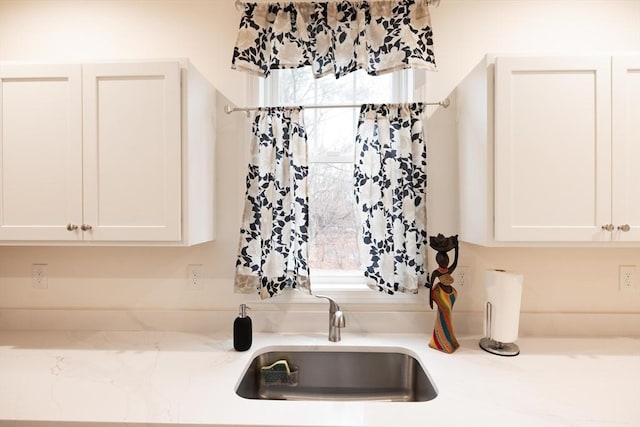 interior details with white cabinetry, sink, and light stone counters