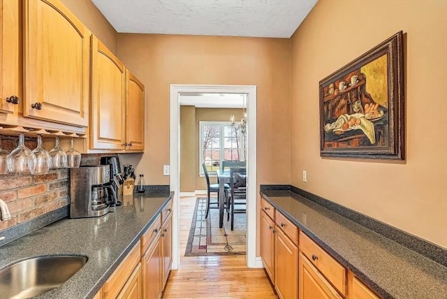 kitchen with a sink, light wood-style floors, dark stone counters, tasteful backsplash, and a textured ceiling