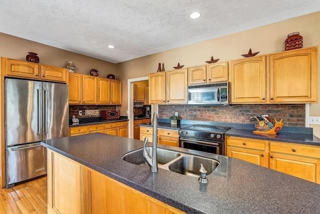kitchen with appliances with stainless steel finishes, dark countertops, a textured ceiling, a sink, and light wood finished floors