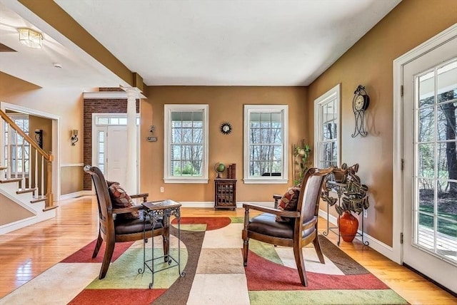 sitting room featuring wood finished floors, stairway, baseboards, and decorative columns