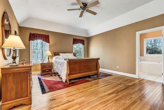 bedroom featuring light wood-type flooring, multiple windows, baseboards, connected bathroom, and lofted ceiling