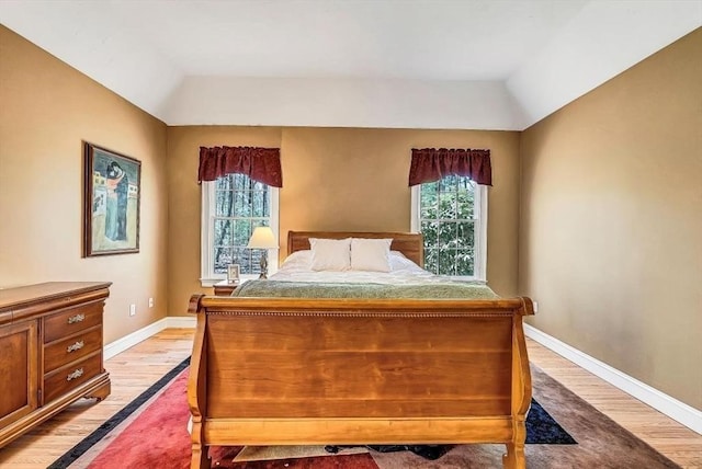 bedroom with multiple windows, light wood-type flooring, baseboards, and lofted ceiling