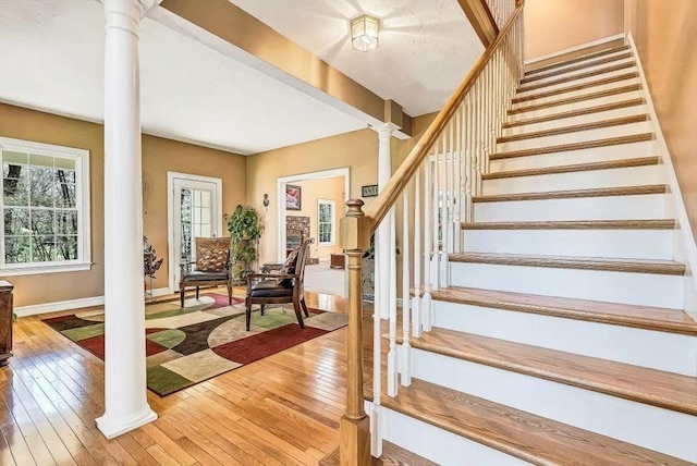stairway featuring ornate columns, hardwood / wood-style floors, and baseboards