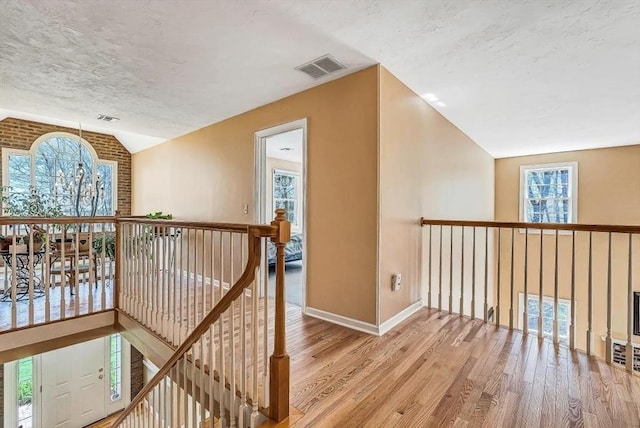corridor featuring vaulted ceiling, light wood-style floors, an upstairs landing, baseboards, and plenty of natural light