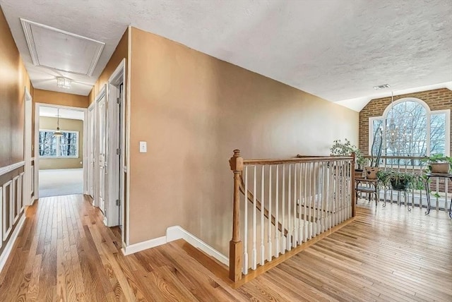 corridor with an upstairs landing, attic access, light wood-style floors, vaulted ceiling, and a textured ceiling