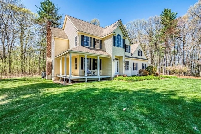 back of house with a chimney, covered porch, a yard, and central AC unit
