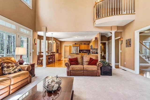 living area featuring decorative columns, a towering ceiling, a chandelier, stairs, and baseboards