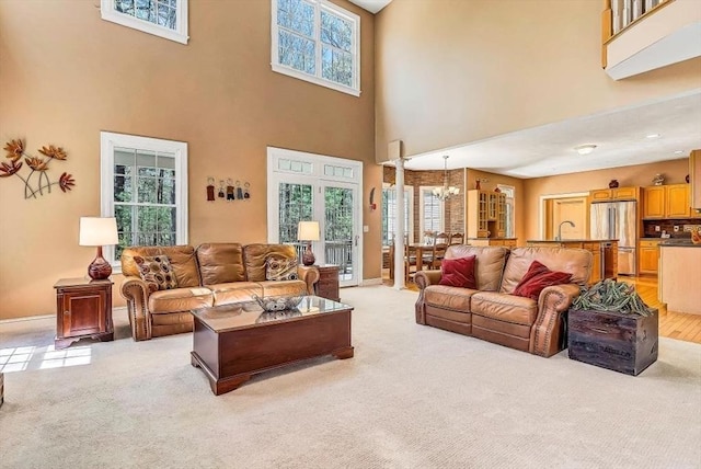 living room featuring light carpet, a high ceiling, a chandelier, and plenty of natural light