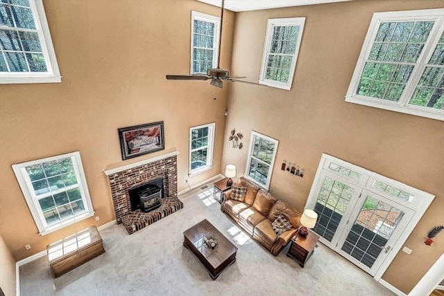 carpeted living area featuring a ceiling fan, a wood stove, a towering ceiling, plenty of natural light, and baseboards
