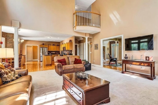 living area featuring decorative columns, a high ceiling, baseboards, and light colored carpet
