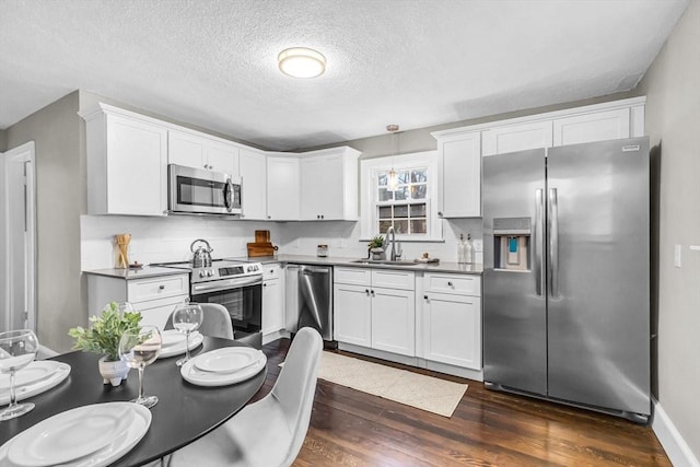 kitchen featuring white cabinetry, hanging light fixtures, appliances with stainless steel finishes, and dark hardwood / wood-style flooring