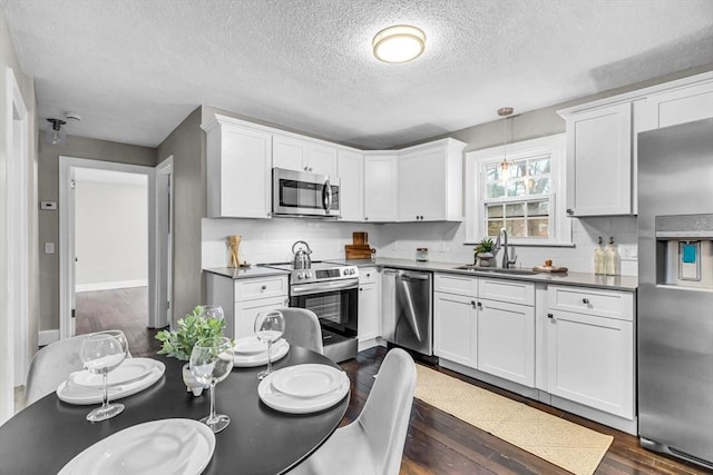 kitchen with hanging light fixtures, sink, white cabinets, dark hardwood / wood-style flooring, and stainless steel appliances