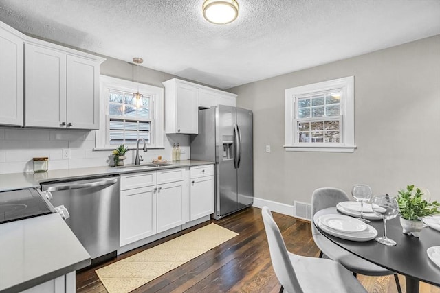 kitchen with white cabinets, stainless steel appliances, sink, backsplash, and hanging light fixtures