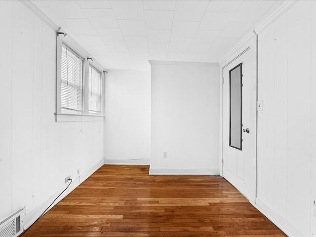 empty room with hardwood / wood-style flooring, wood walls, and a baseboard radiator