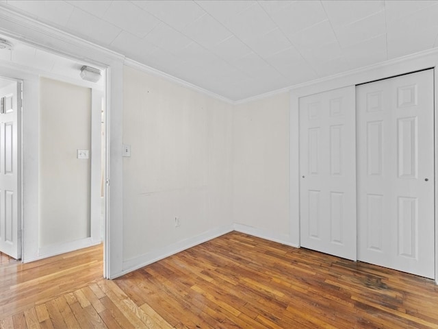 unfurnished bedroom with a closet, hardwood / wood-style floors, and crown molding