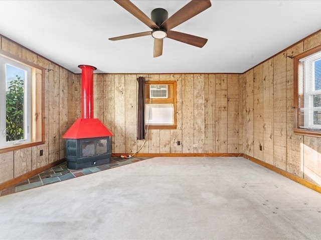 spare room with dark colored carpet, ceiling fan, a wood stove, and wooden walls