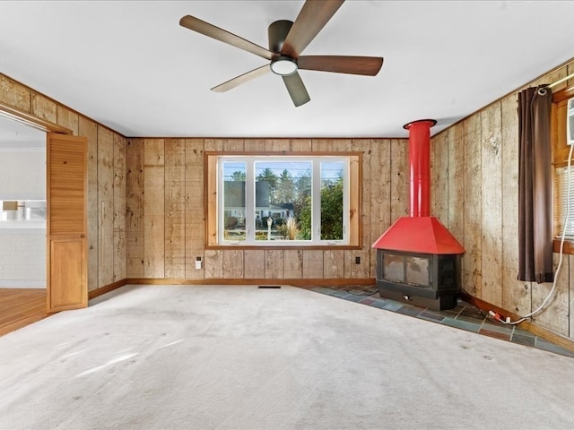 miscellaneous room with a wood stove, wooden walls, ceiling fan, and dark colored carpet