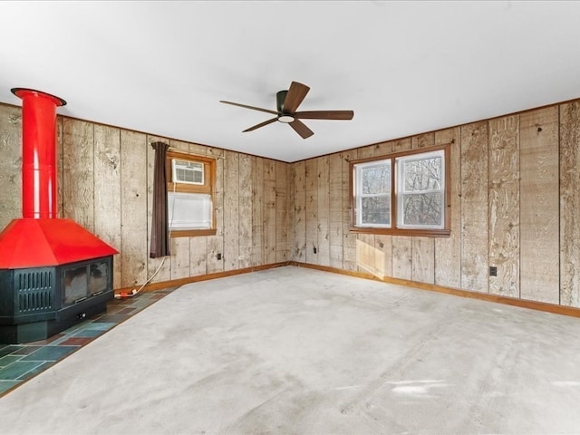 spare room with ceiling fan, a wall unit AC, a wood stove, and wooden walls