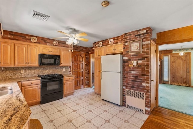 kitchen featuring light stone countertops, visible vents, brick wall, radiator heating unit, and black appliances