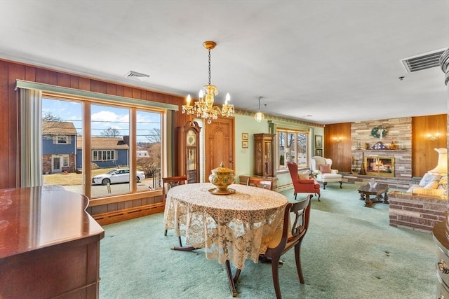 carpeted dining room featuring a stone fireplace, wooden walls, visible vents, and a chandelier