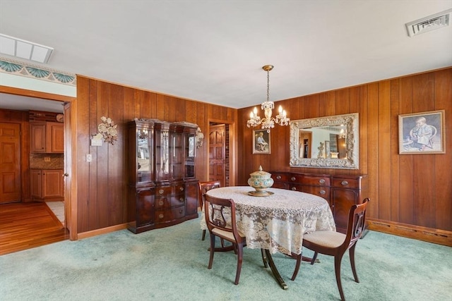 dining room with visible vents, light colored carpet, wood walls, and a notable chandelier