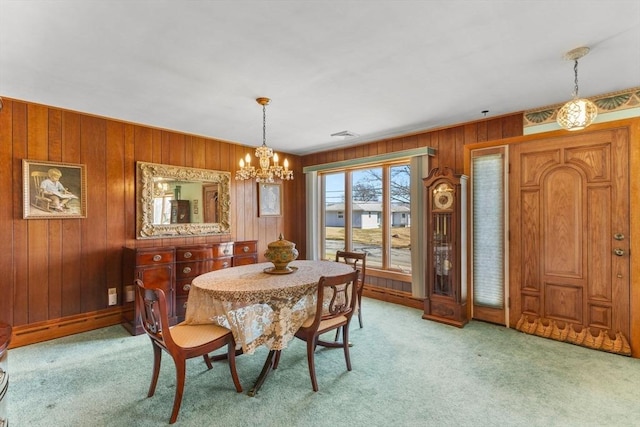 dining area featuring light colored carpet, an inviting chandelier, and wooden walls