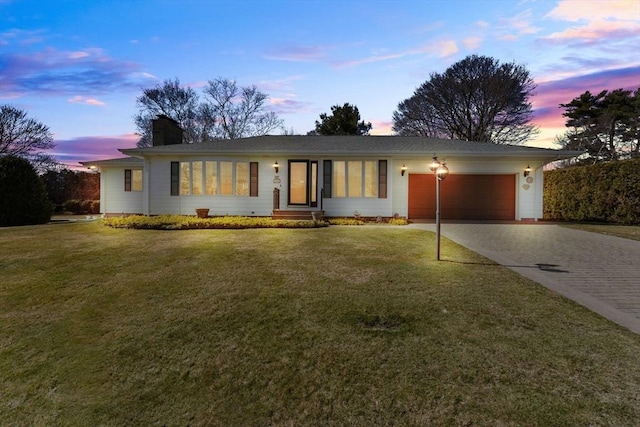 ranch-style home featuring an attached garage, a front yard, a chimney, and driveway