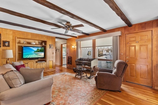 living room with wooden walls, built in features, wood finished floors, ceiling fan, and beamed ceiling