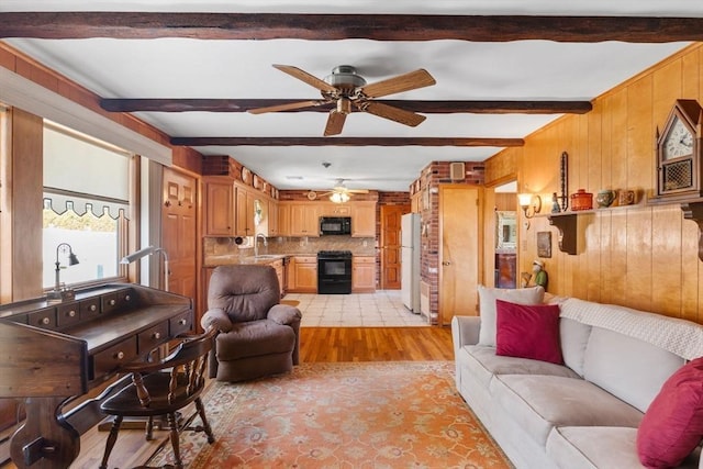 living area featuring light wood-style floors, beamed ceiling, wooden walls, and a ceiling fan